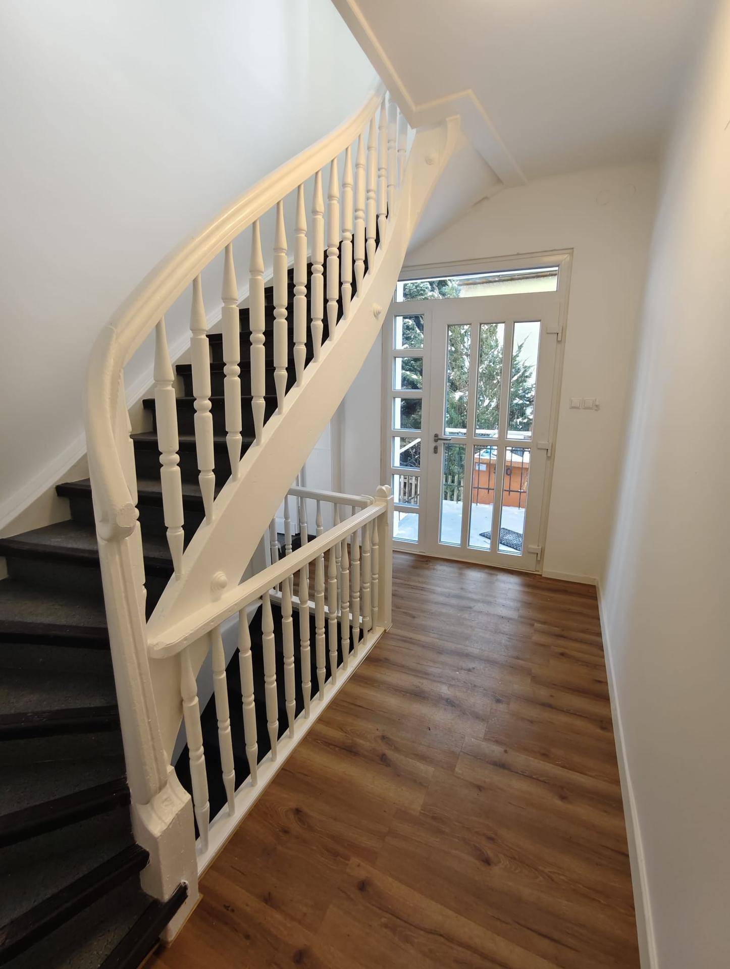 Heller Flur mit eleganter Holztreppe und einer Glastür, die ins Freie führt.