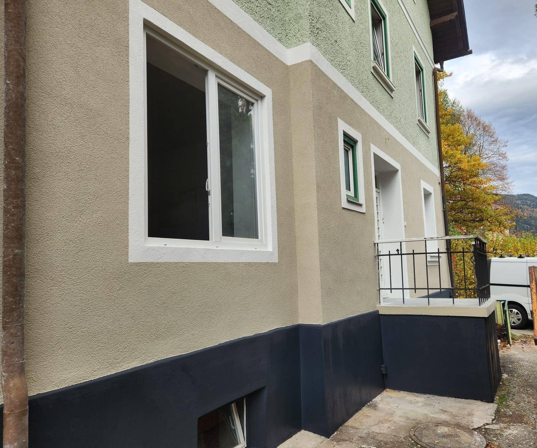 Detailansicht der Gebäudefassade mit einem Fenster, Eingangsbereich und dunklem Sockel.
