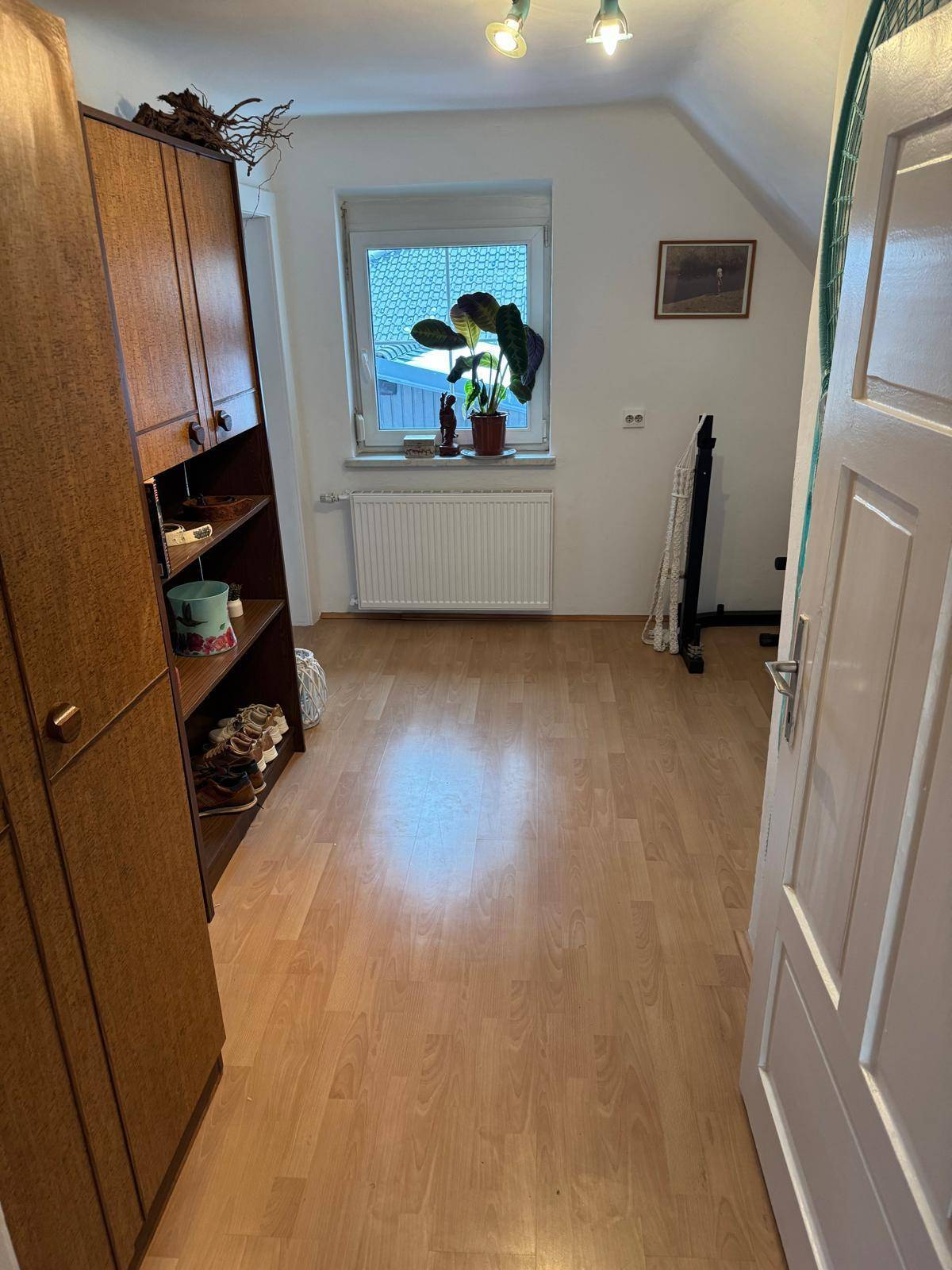 Helles Schlafzimmer im Dachgeschoss mit Laminatboden, Schrank und Fenster mit Ausblick.