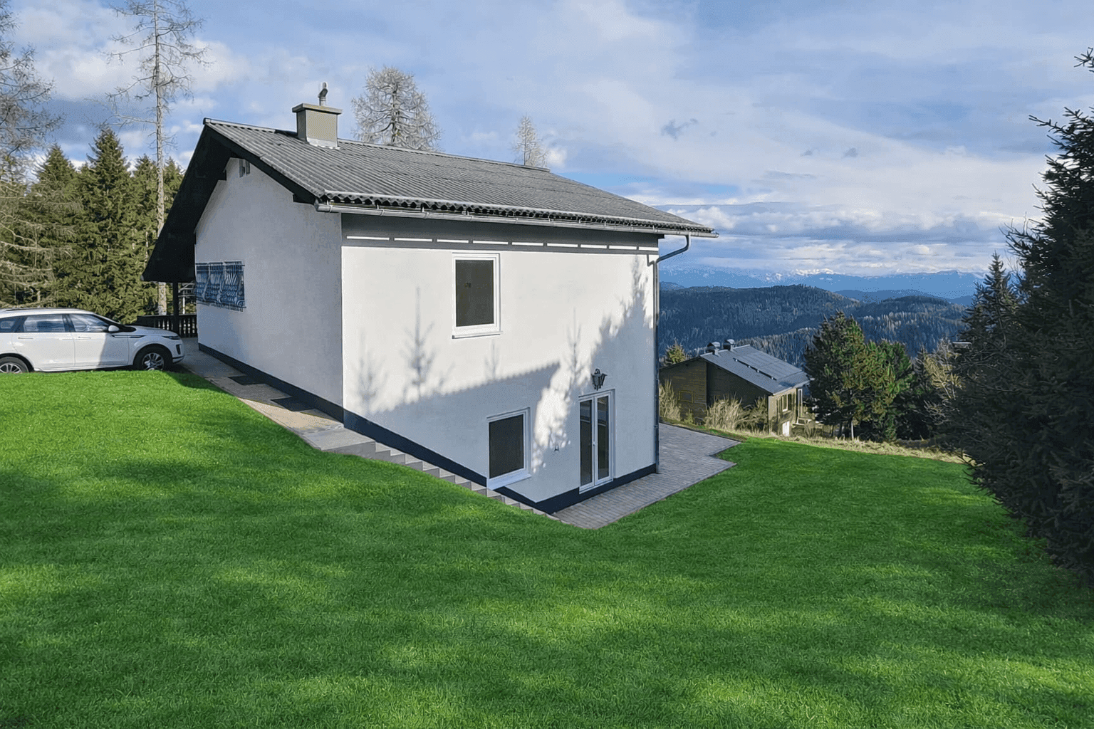 Rückansicht des Hauses mit gepflegtem Rasen und Blick auf die umliegende Berglandschaft.