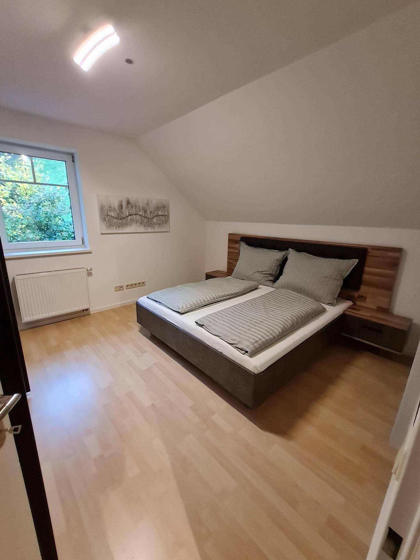 Gemütliches Schlafzimmer im Dachgeschoss mit Holzboden, Doppelbett und Fenster mit Blick ins Grüne.