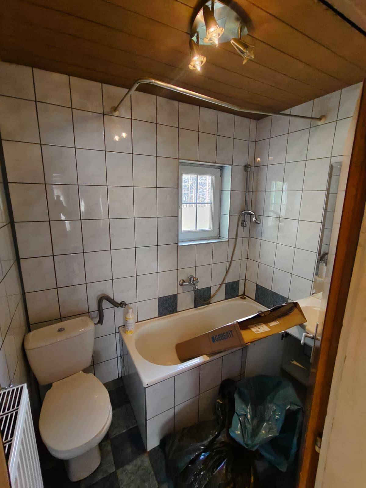 Badezimmer mit Badewanne, Toilette, Waschbecken und Fenster, gekennzeichnet durch zweifarbige Fliesen.