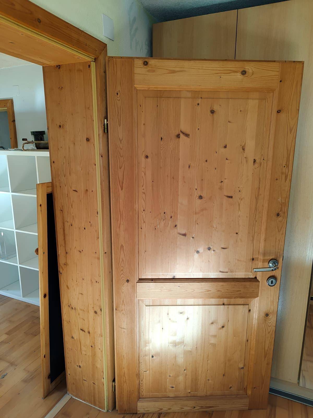 Eine schlichte Holztür aus hellem Kiefernholz mit einfacher Klinke, die zu einem Raum führt.