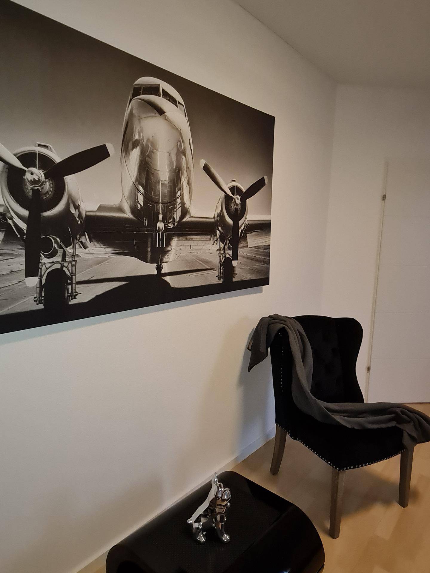 Elegante Sitzecke mit schwarzem Sessel und großem Schwarz-Weiß-Bild eines Flugzeugs.