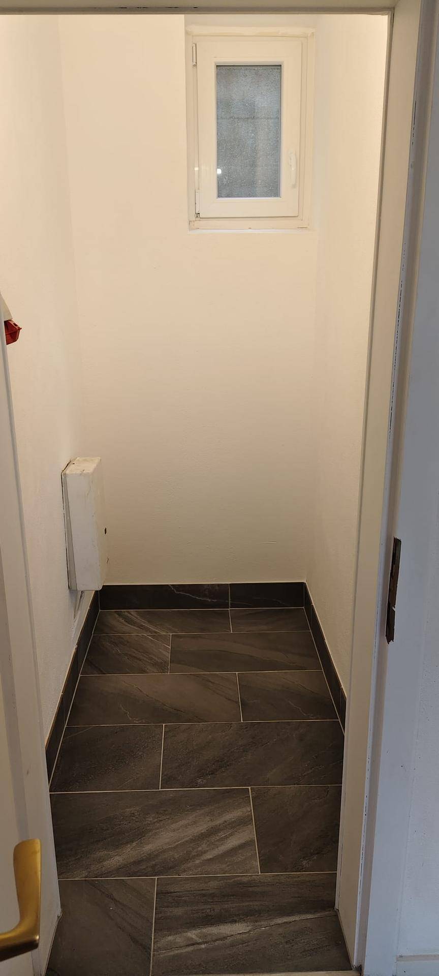 Kleiner Raum mit Fliesenboden und Fenster, ideal als Abstell- oder Hauswirtschaftsraum.