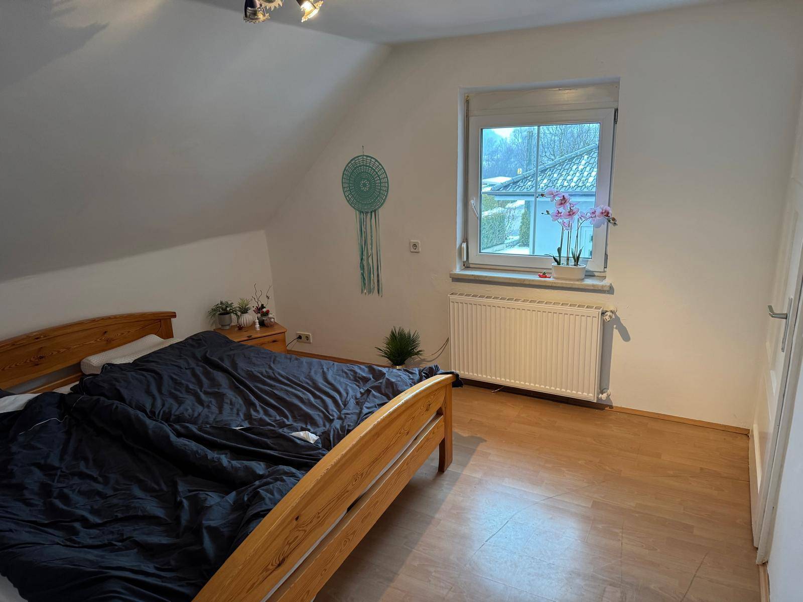 Gemütliches Schlafzimmer im Dachgeschoss mit Holzbett, Laminatboden und Fenster.