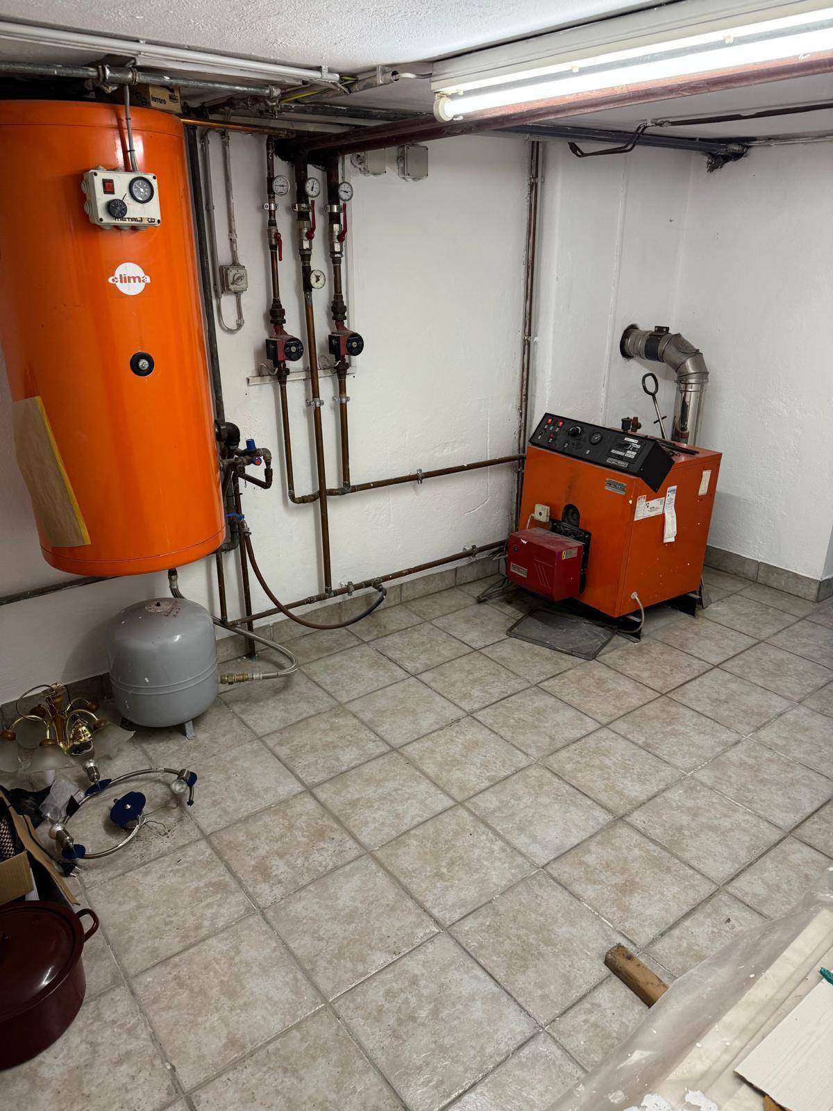 Heizraum im Keller mit großem Warmwasserspeicher und Heizkessel auf Fliesenboden.