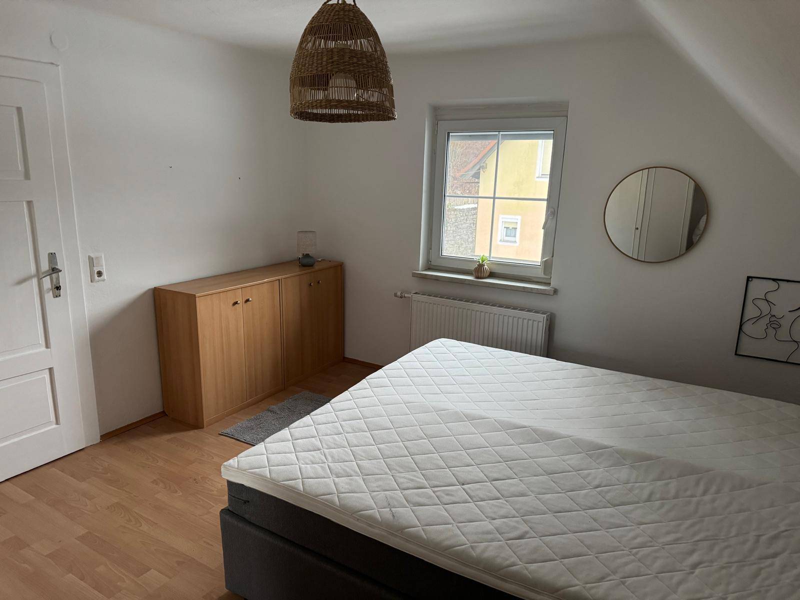 Schlafzimmer im Dachgeschoss mit schräger Decke, Bett und einem Fenster mit Blick nach draußen.
