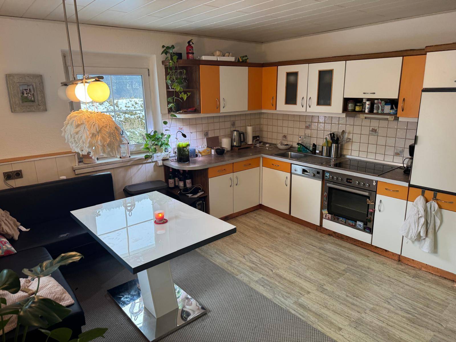 Funktionale Küche mit orange-weißen Schränken, Essbereich und Fenster mit Ausblick.