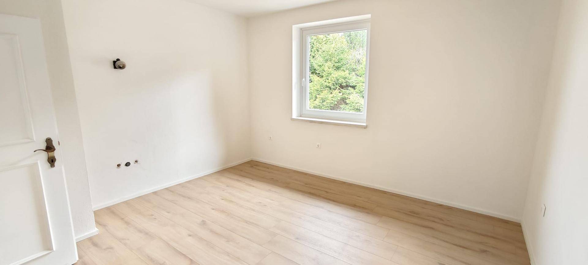 Helles Schlafzimmer mit Laminatboden und Fenster mit Blick ins Grüne.