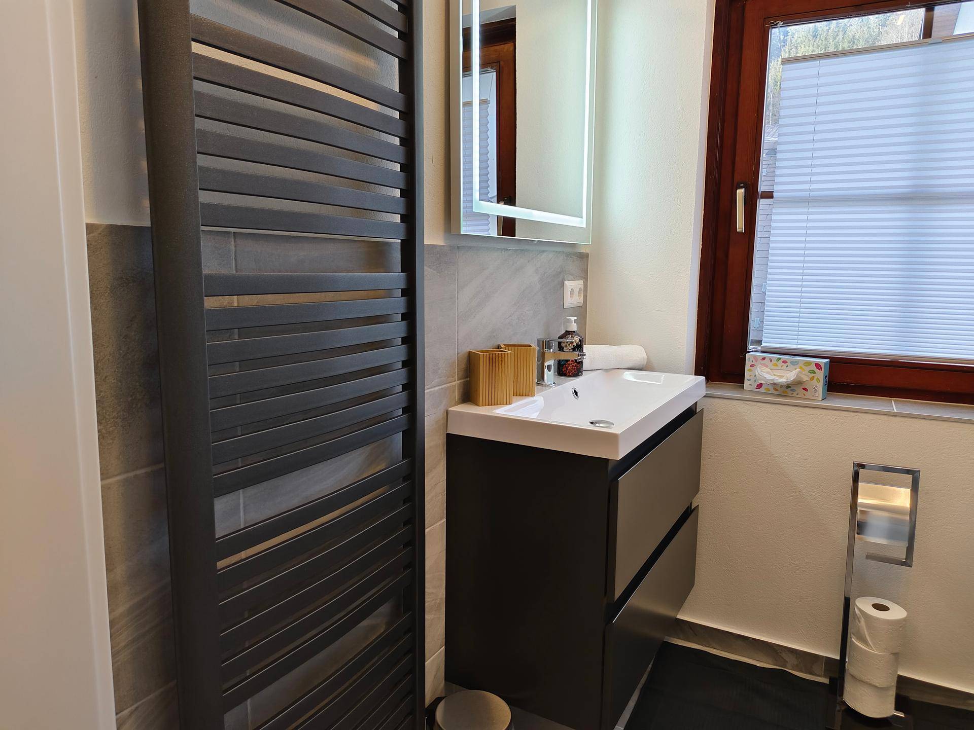 Modernes Badezimmer mit Waschtisch, beleuchtetem Spiegelschrank und beheiztem Handtuchhalter.