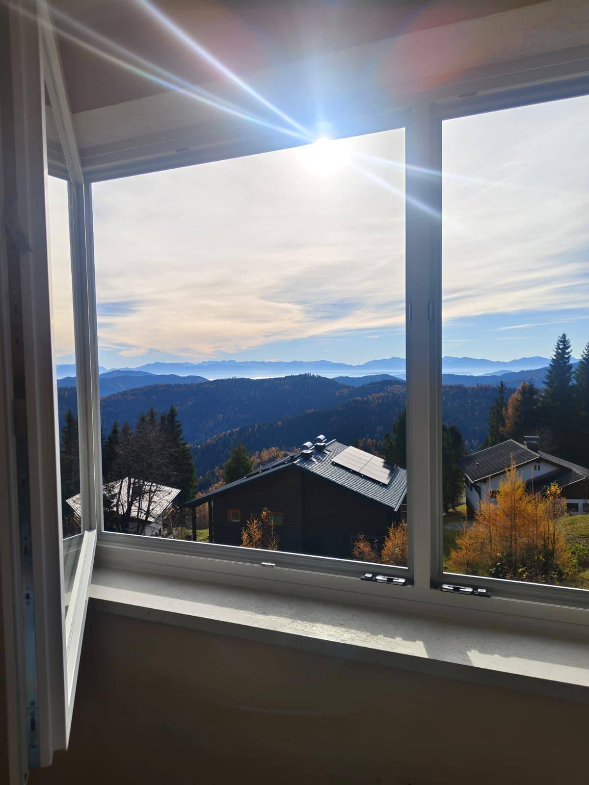 Sonnenverwöhnter Ausblick aus dem Fenster auf die malerische Berglandschaft und umliegende Häuser.