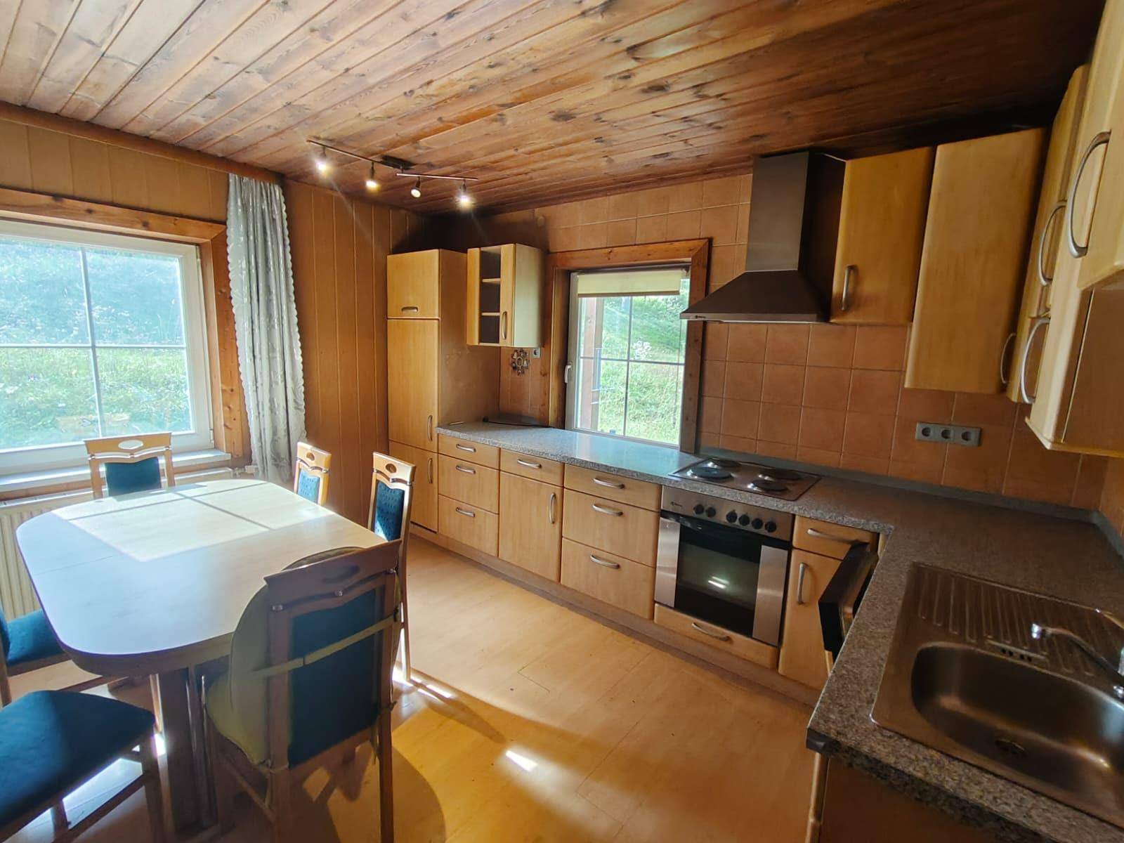 Gemütliche Küche mit Holzschränken, Esstisch und Blick ins Grüne durch die Fenster.