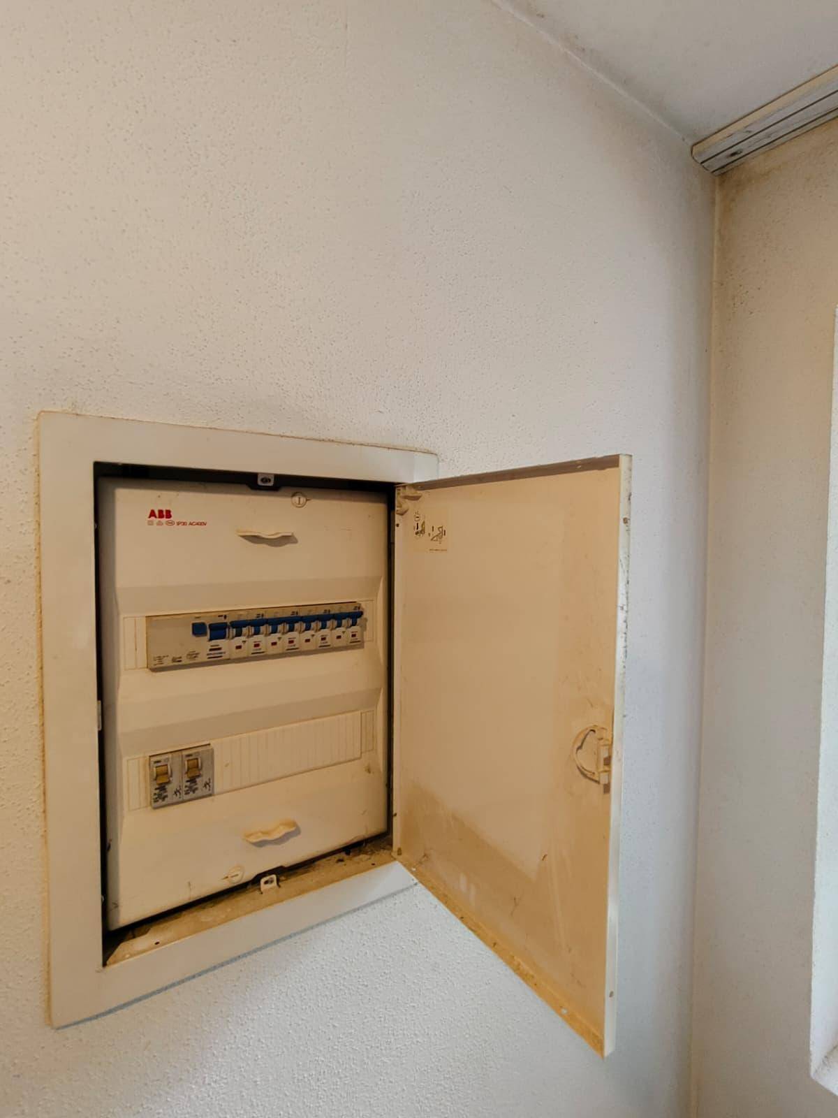 Ein geöffneter Sicherungskasten an einer weißen Wand, der die elektrische Installation zeigt.
