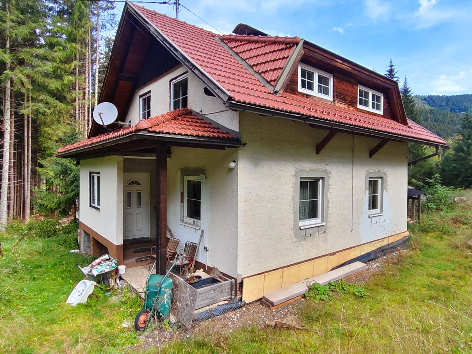 Ländliches Haus mit rotem Ziegeldach und heller Fassade, umgeben von Wald und Natur.