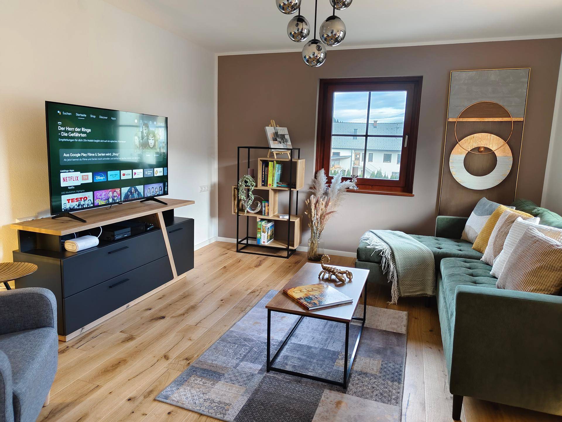 Modern eingerichtetes Wohnzimmer mit großem Fernseher, bequemer Couch und Holzboden.