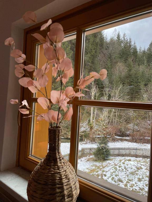 Fensterblick auf eine verschneite Waldlandschaft, mit einer dekorativen Vase auf der Fensterbank.