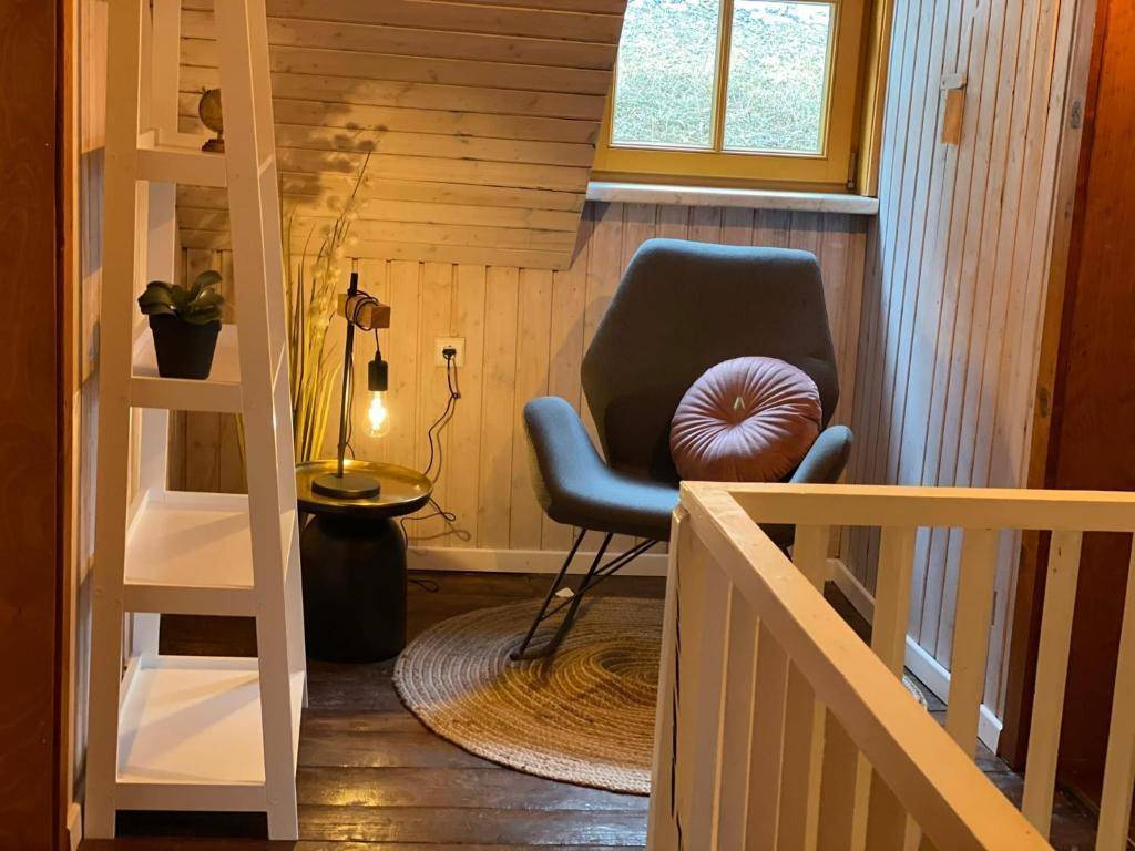 Gemütlicher Dachbodenbereich mit schrägen Holzwänden, Sessel, Beistelltisch mit Lampe und Fenster.