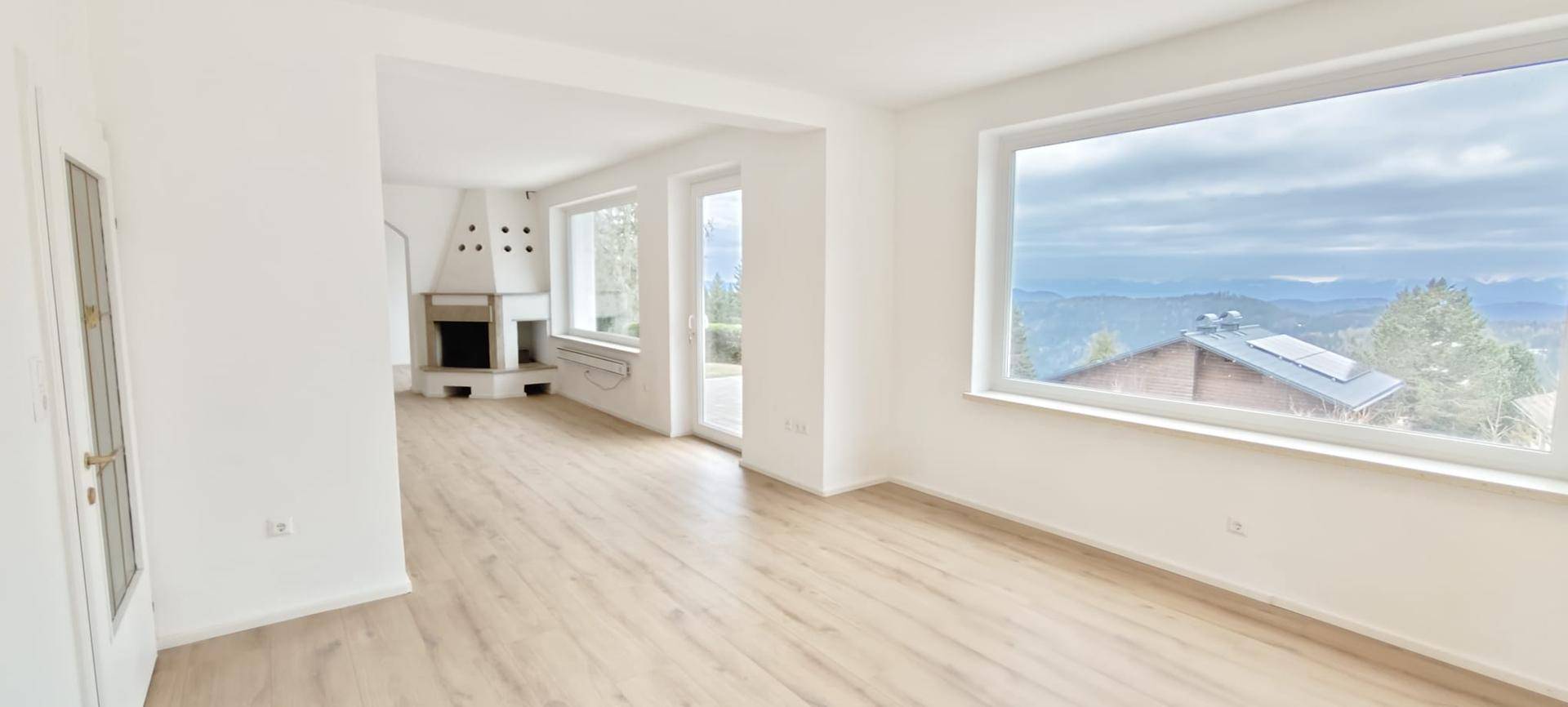 Heller Wohnbereich mit Kamin, Laminatboden und großen Fenstern mit Bergblick.
