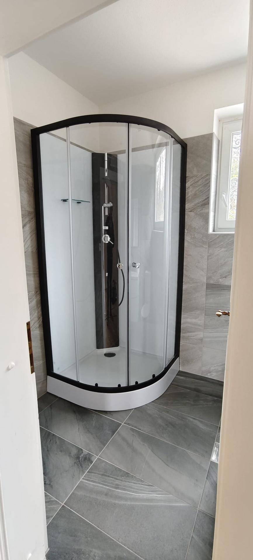 Modernes Badezimmer mit großer Duschkabine und eleganten grauen Fliesen.