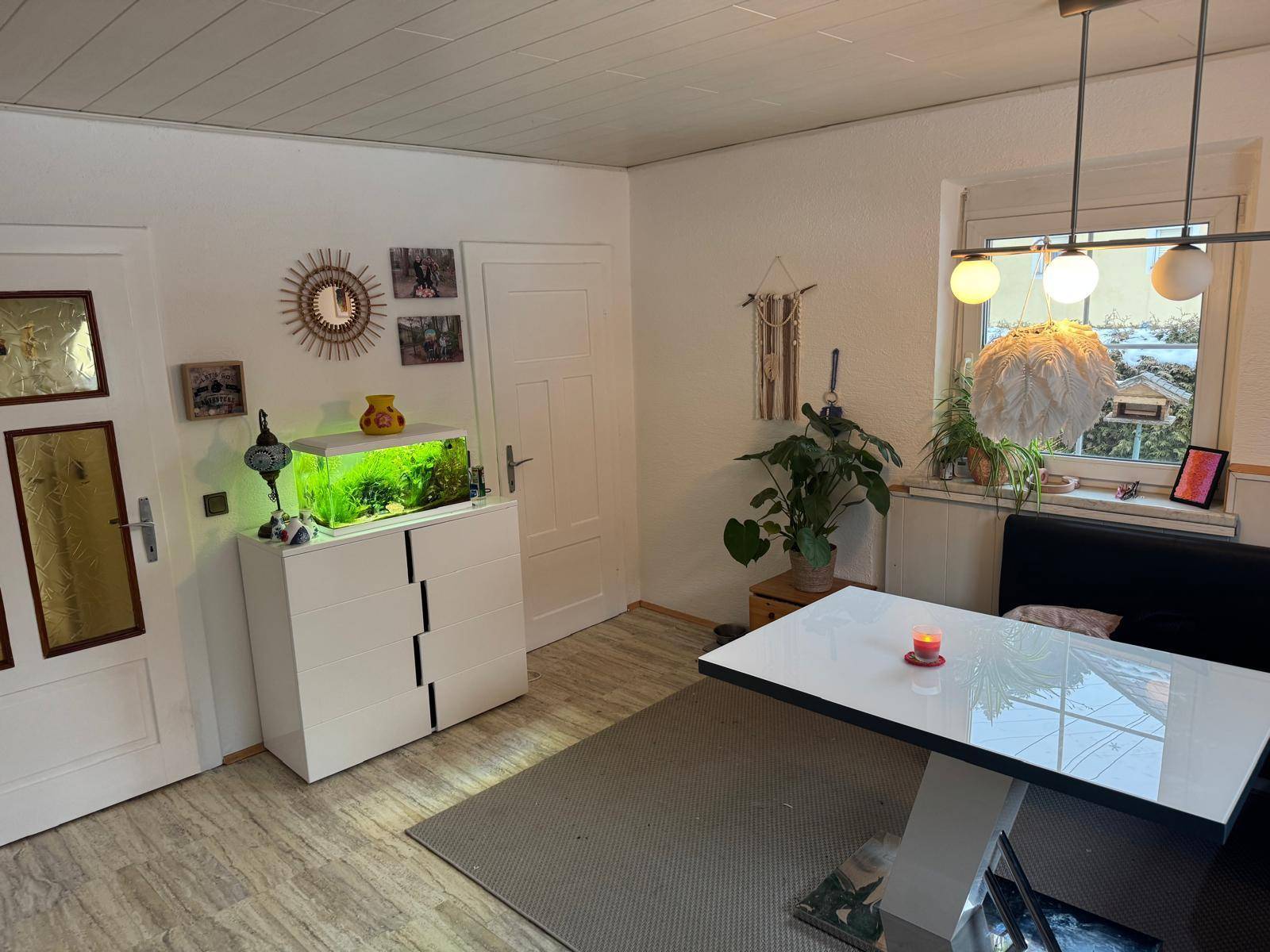 Heller Wohn- und Essbereich mit modernem Tisch, Aquarium und Blick ins Grüne.