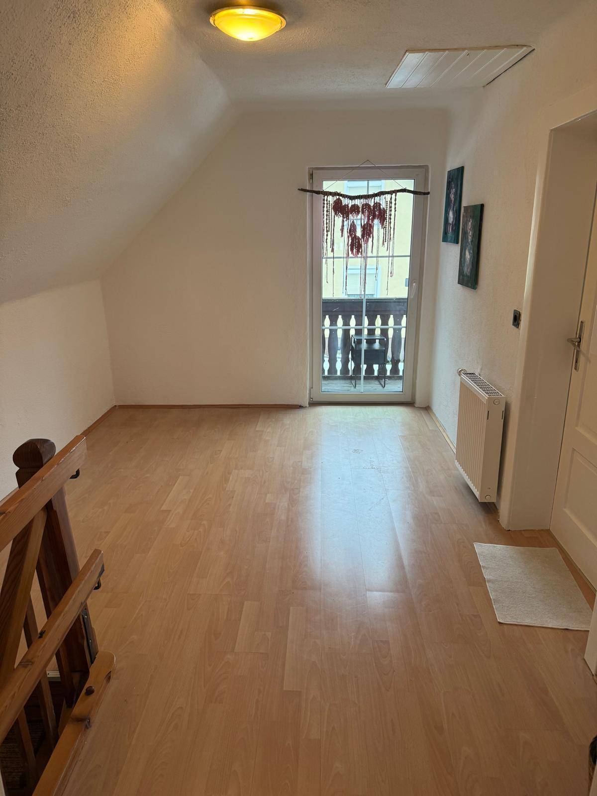Heller Flur im Dachgeschoss mit Laminatboden und Zugang zu einem kleinen Balkon.