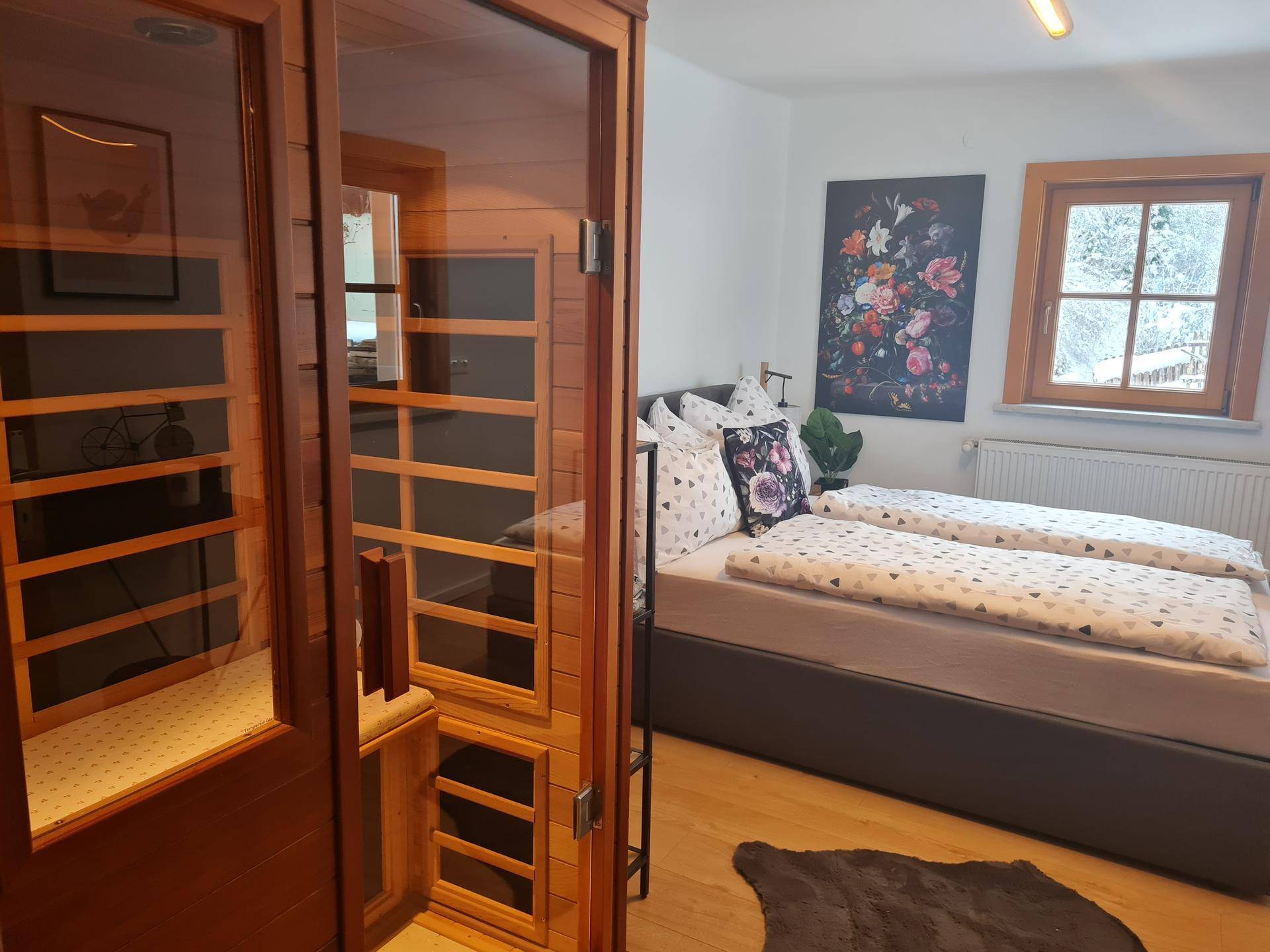 Gemütliches Schlafzimmer mit Doppelbett, Holzboden und integrierter Sauna, Blick auf verschneite Landschaft.