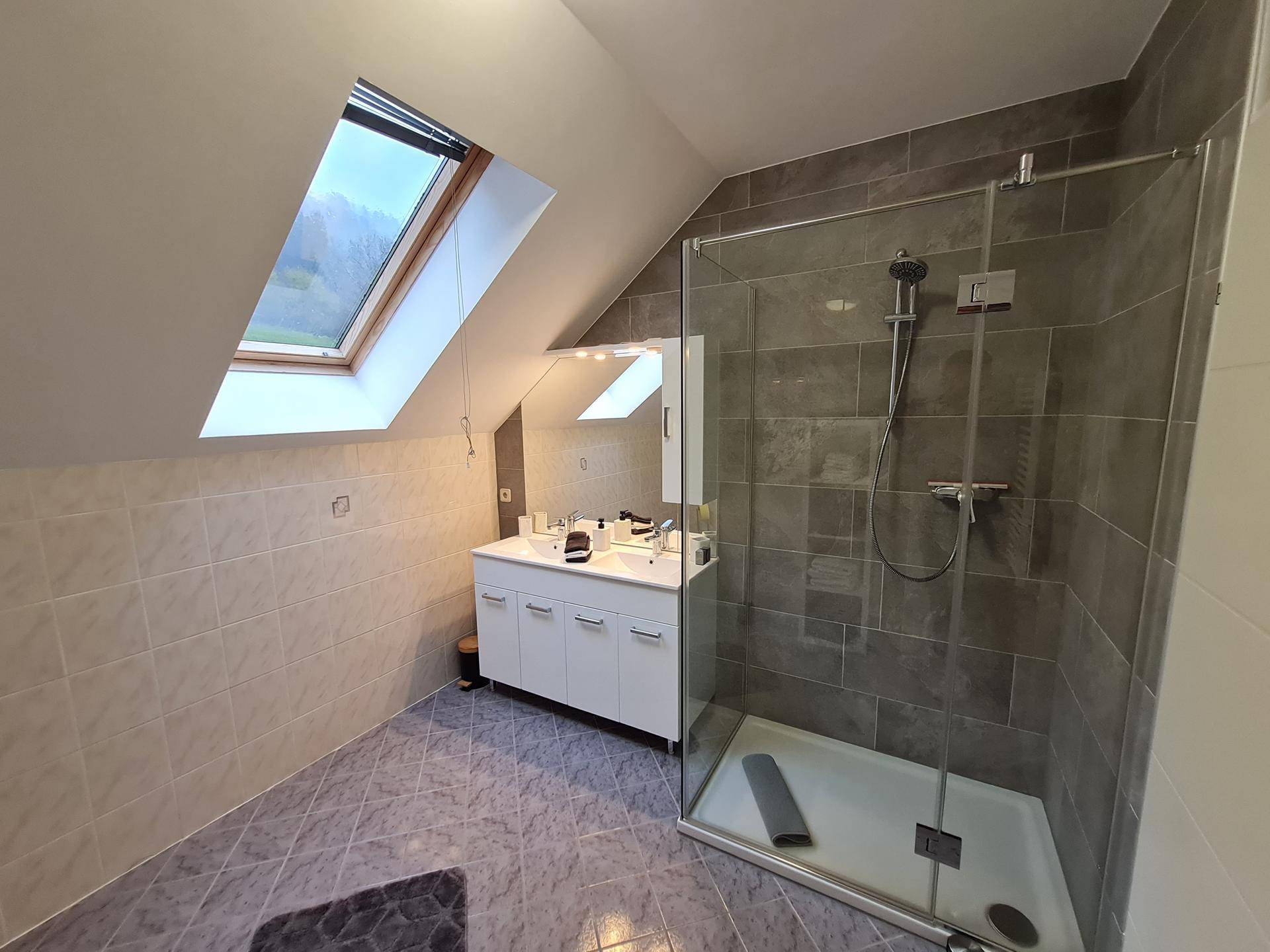 Helles Badezimmer im Dachgeschoss mit Schrägdach, Dachfenster, Doppelwaschbecken und Duschkabine.