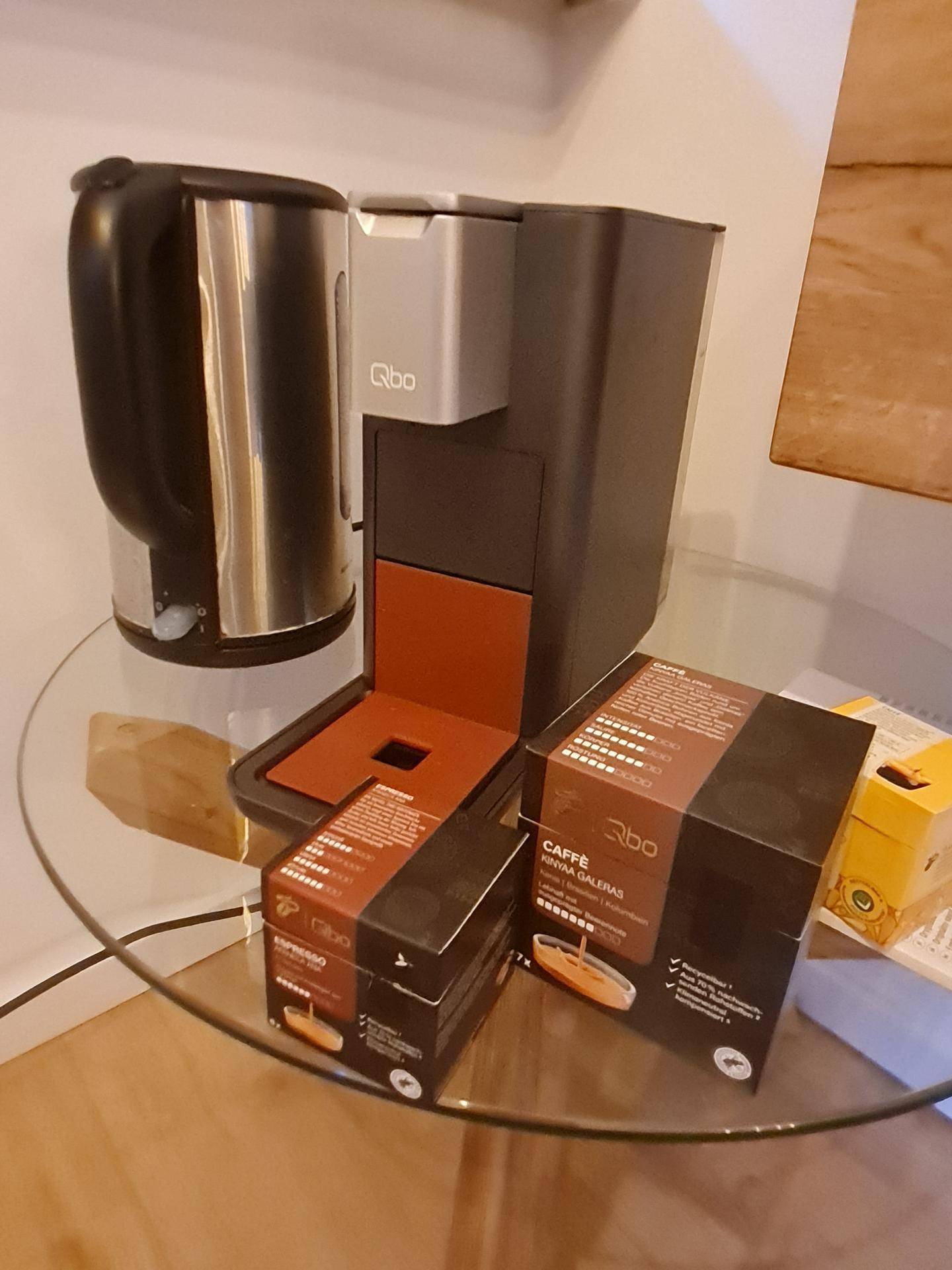 Kaffeemaschine und Wasserkocher auf einem Glastisch mit Kaffeekapseln für den täglichen Genuss.