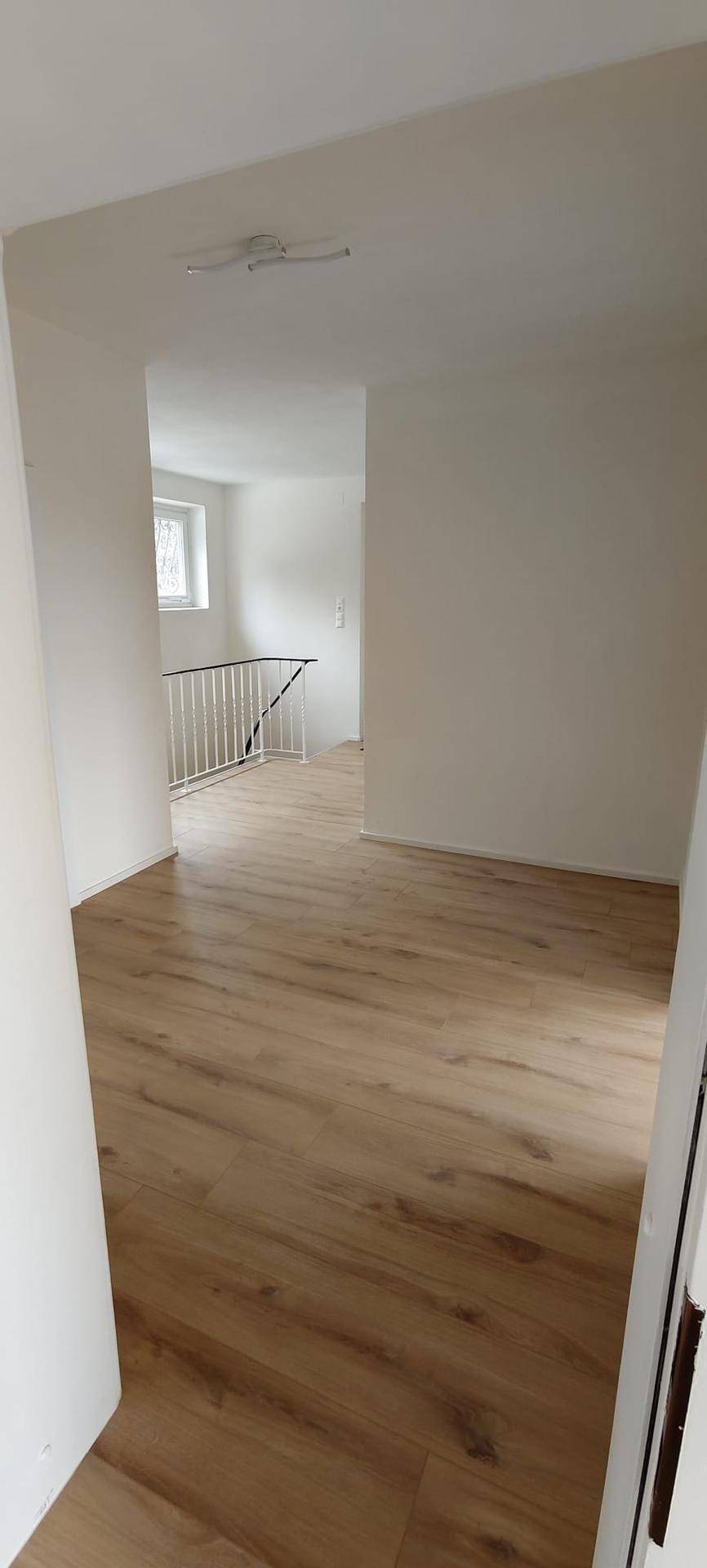 Heller Flur mit modernem Laminatboden und Treppengeländer, der zu weiteren Räumen führt.