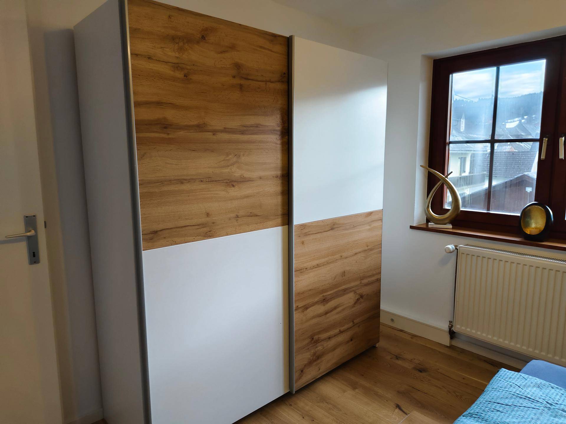 Schlafzimmer mit großem Schiebetürenschrank in Holzoptik und Fenster mit Blick ins Grüne.