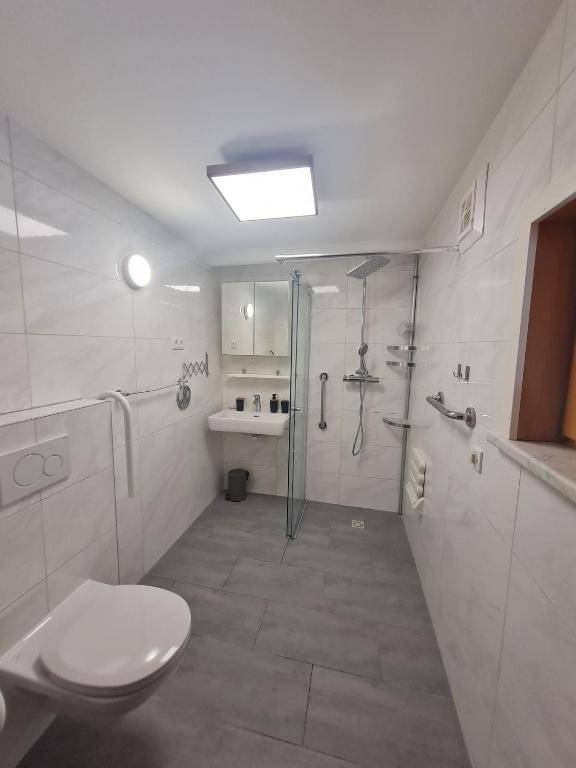 Modernes Badezimmer mit barrierefreier Dusche, Wand-WC, Haltegriffen und hellen Fliesen.