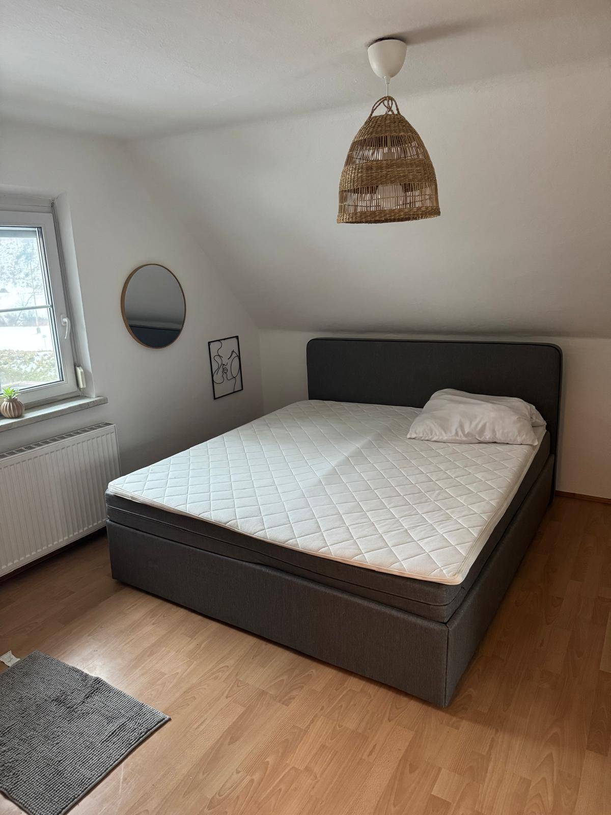 Schlafzimmer im Dachgeschoss mit schräger Decke, Doppelbett und einem Fenster für Tageslicht.