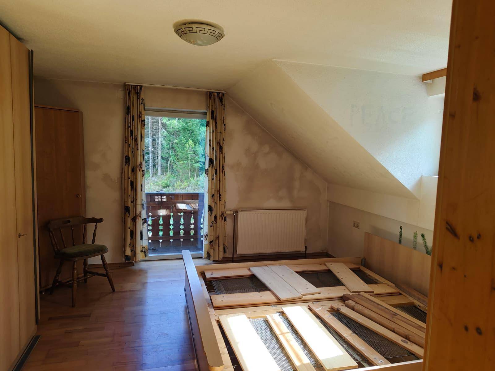 Dachschlafzimmer mit Bettgestell, Kleiderschrank und Balkonzugang, vor der Renovierung.