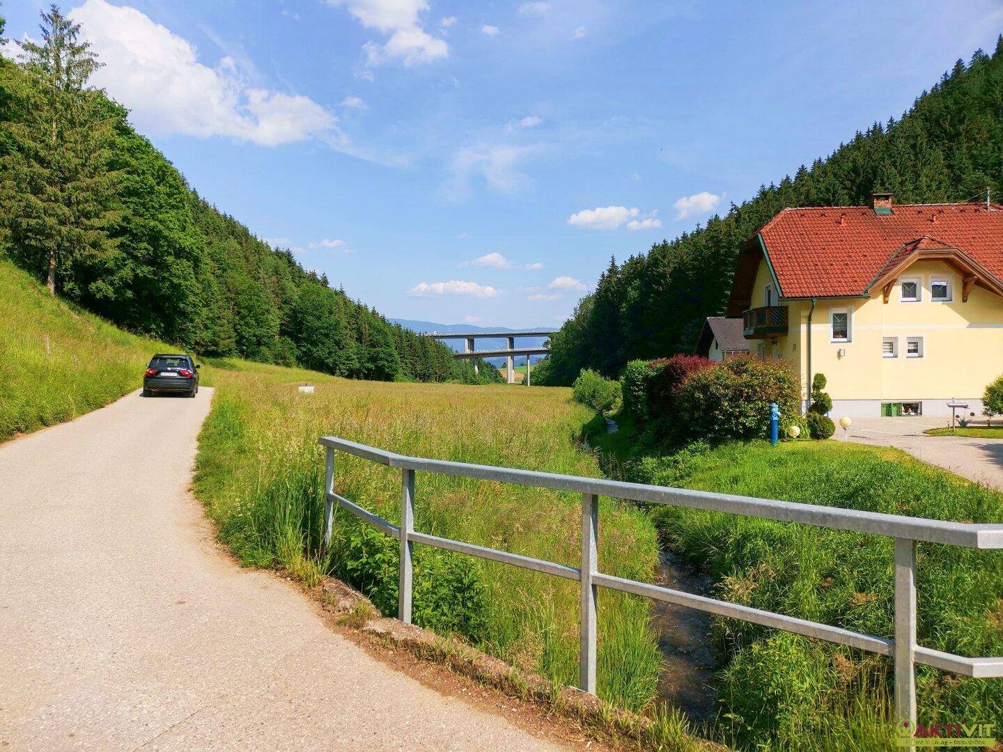 Idyllische ländliche Umgebung mit einem Haus, einer Straße und einer Brücke im Hintergrund.