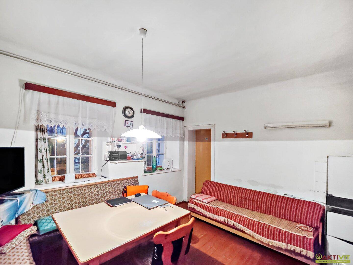 Gemütlicher Wohnbereich mit Esstisch, Sofa und Fenstern mit Vorhängen.