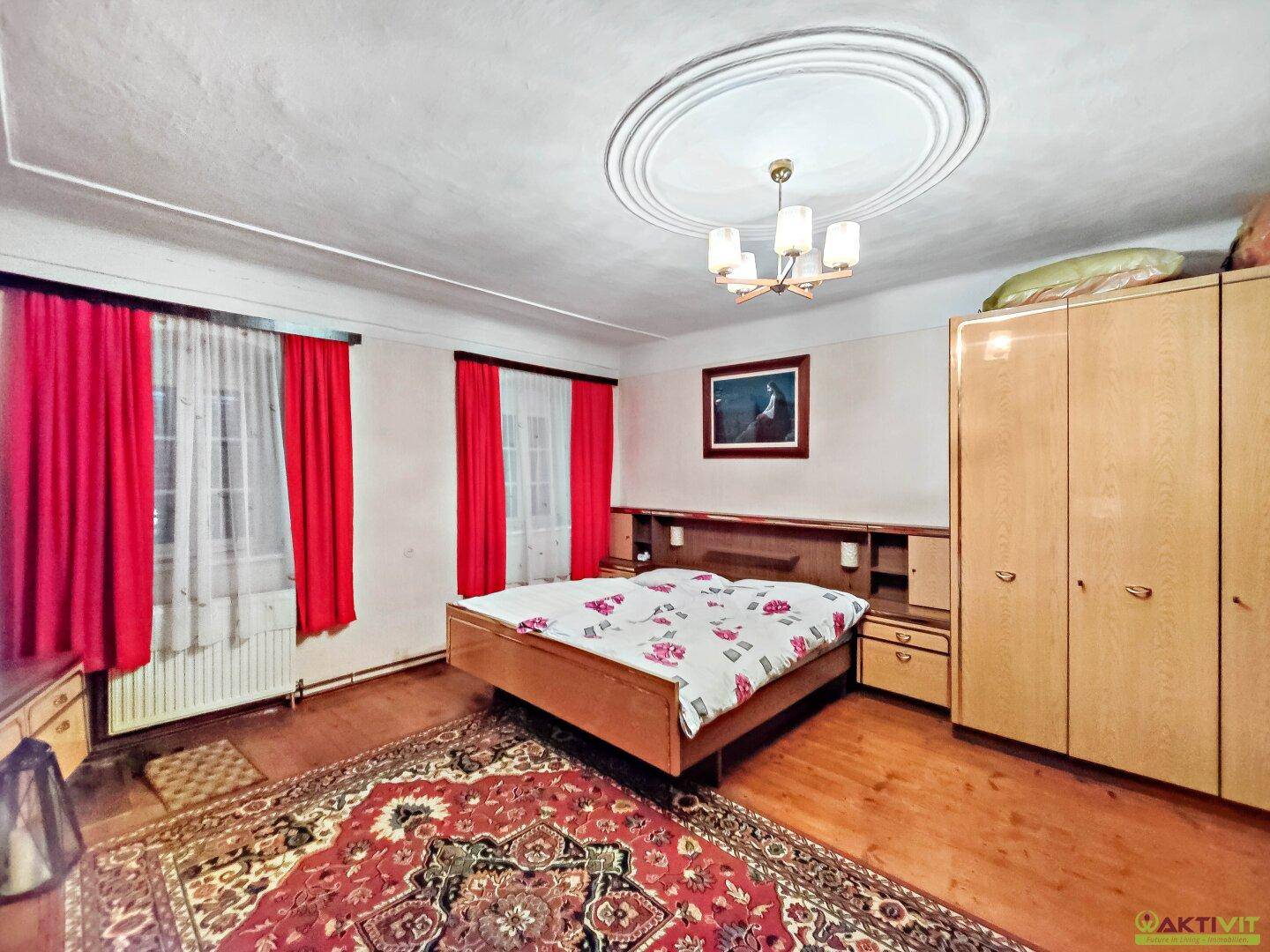 Schlafzimmer mit Doppelbett, Holzschrank und dekorativer Stuckdecke.
