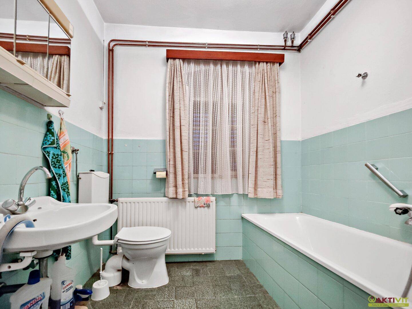 Badezimmer im Stil der 80er Jahre mit hellblauen Fliesen, Badewanne und Fenster.