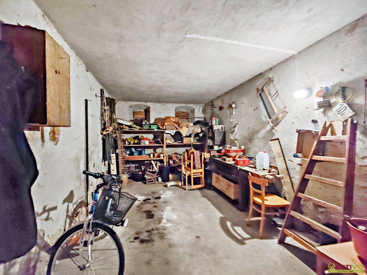 Unaufgeräumter Kellerraum mit Werkzeugen, Fahrrädern und Lagerregalen.