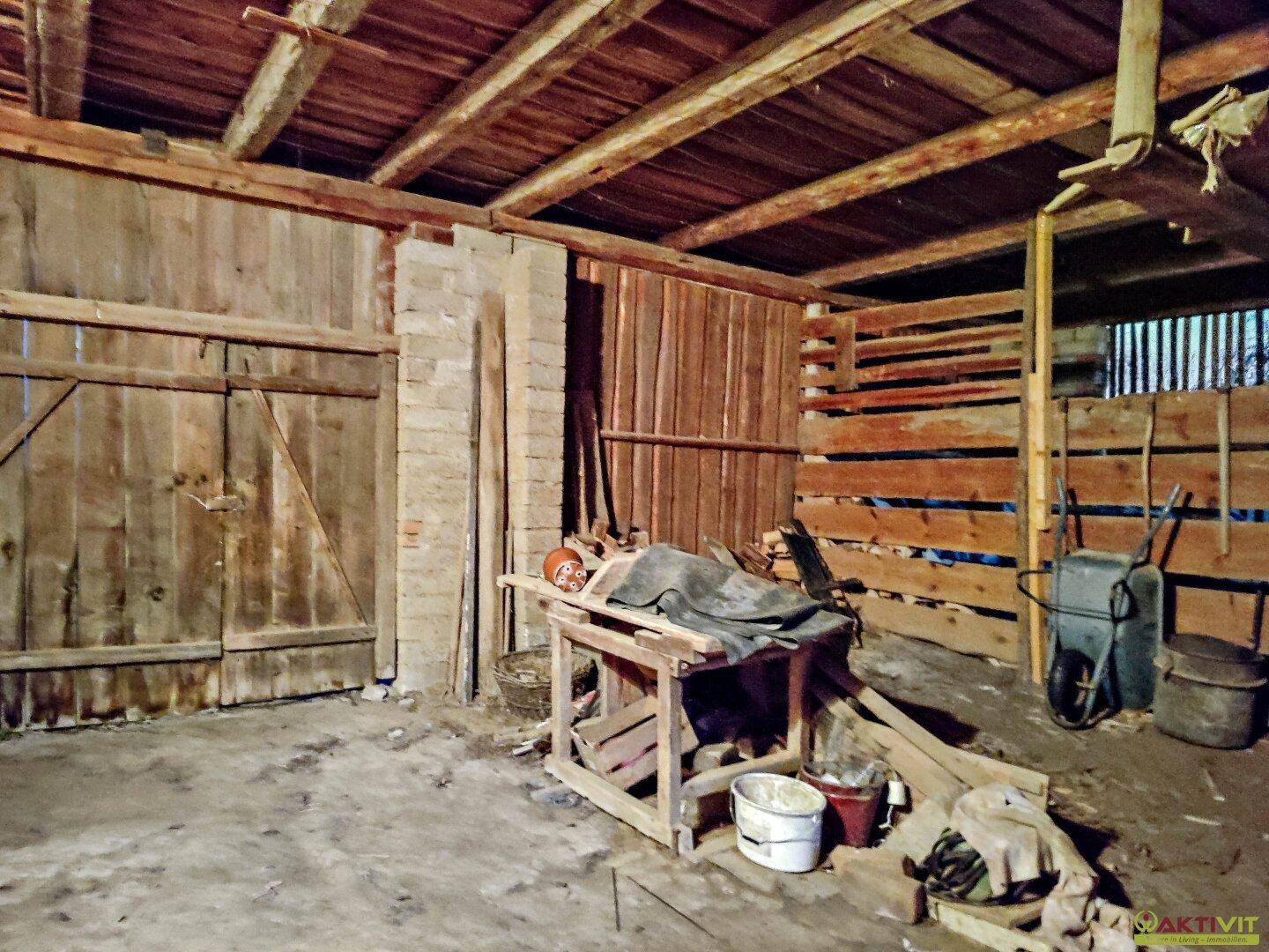 Rustikale Scheune mit Holzwänden, Holzbalken und verschiedenen Geräten.