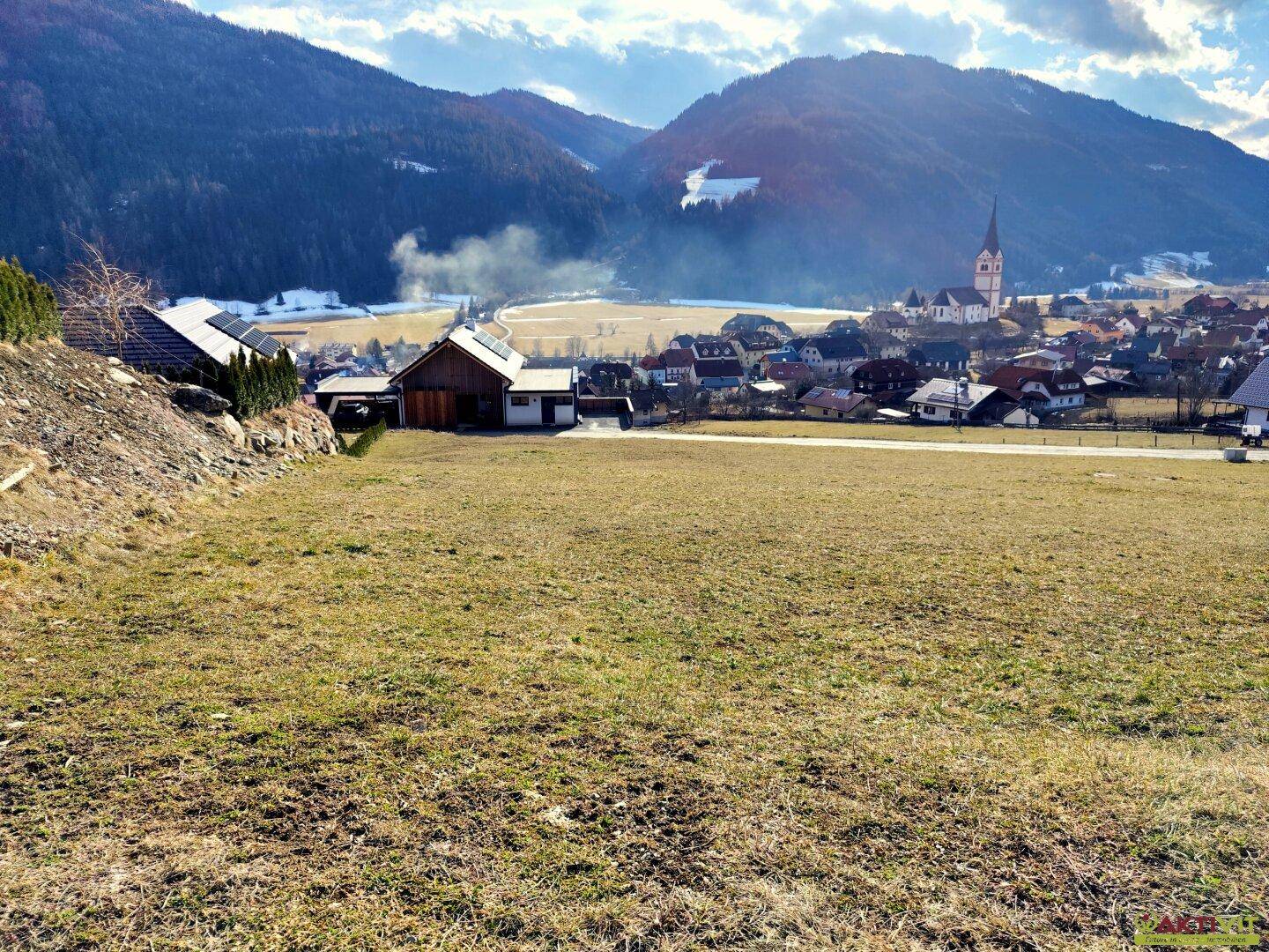Weitläufiger Ausblick auf ein malerisches Dorf in einem Tal, umgeben von Bergen.