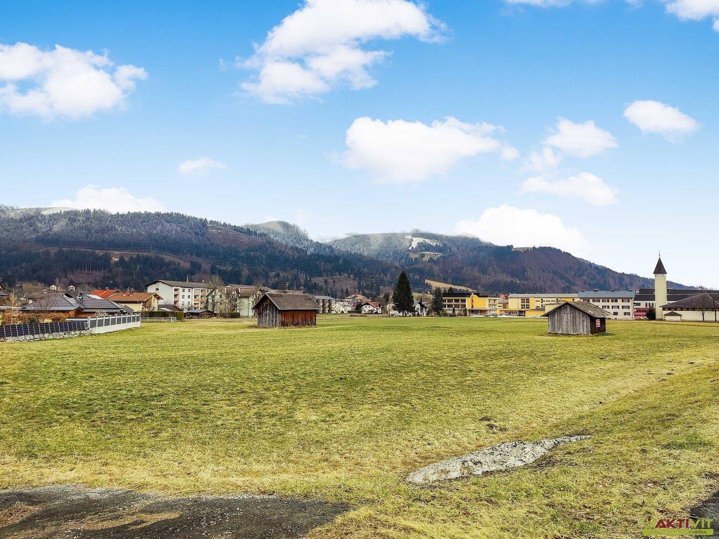 Panoramablick über ein weites Feld mit schneebedeckten Bergen und vereinzelten Gebäuden am Horizont.