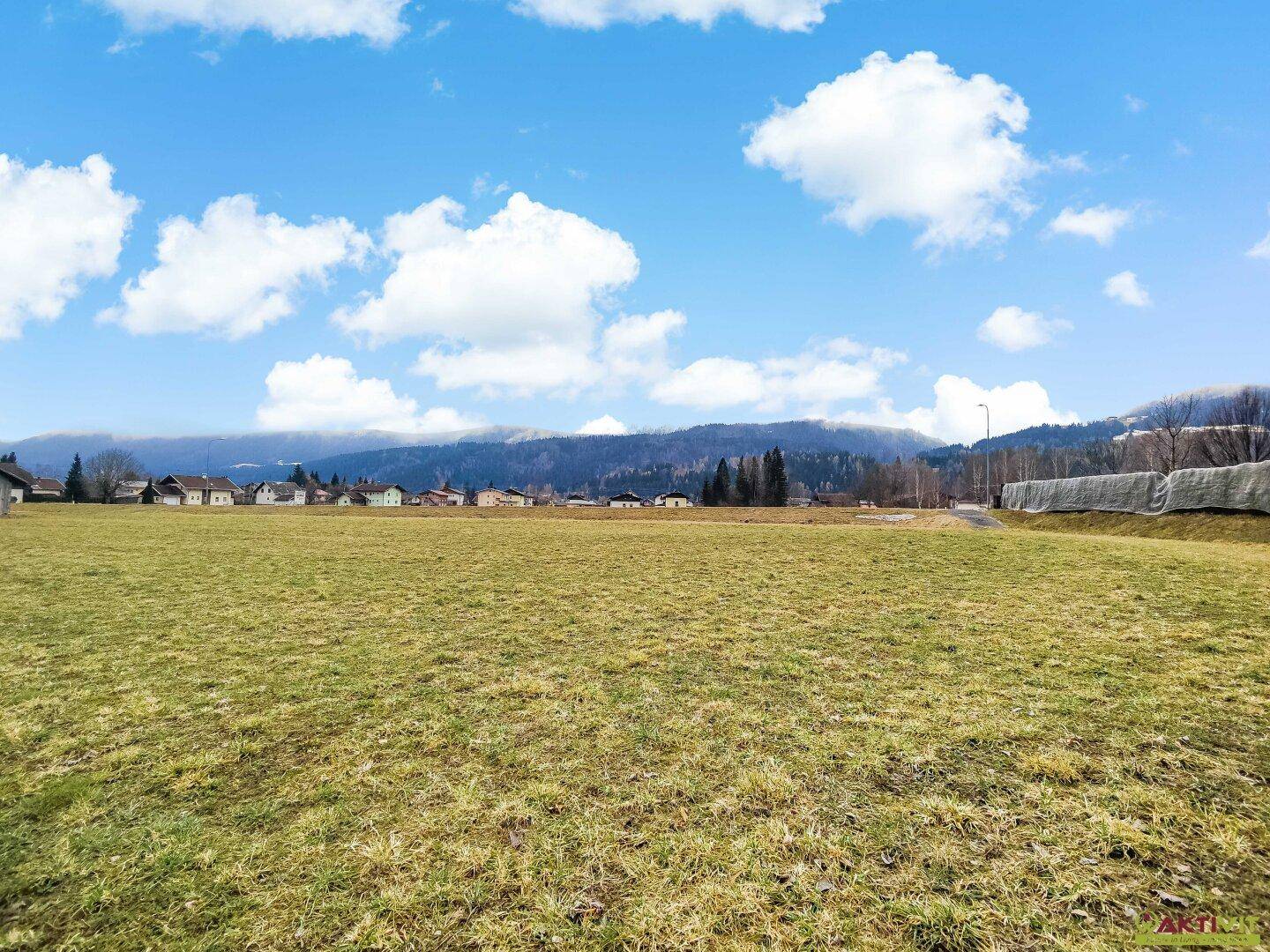 Ausgedehnte Grünfläche mit Fernsicht auf eine Siedlung und die bewaldeten Hügelketten in der Ferne.
