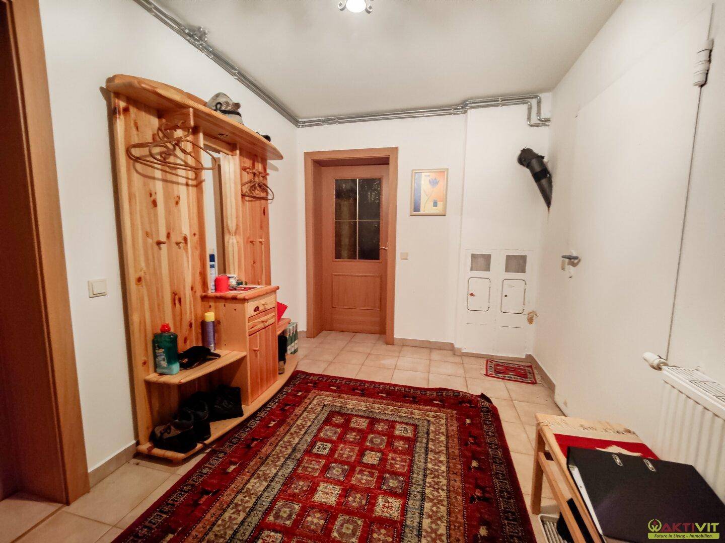 Gemütlicher Eingangsbereich mit Holzgarderobe, Fliesenboden und traditionellem Teppich.