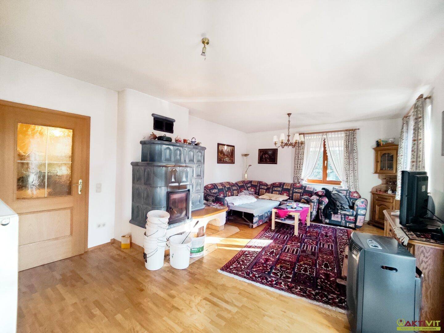 Geräumiges Wohnzimmer mit Kachelofen, Parkettboden und gemütlicher Sitzecke.