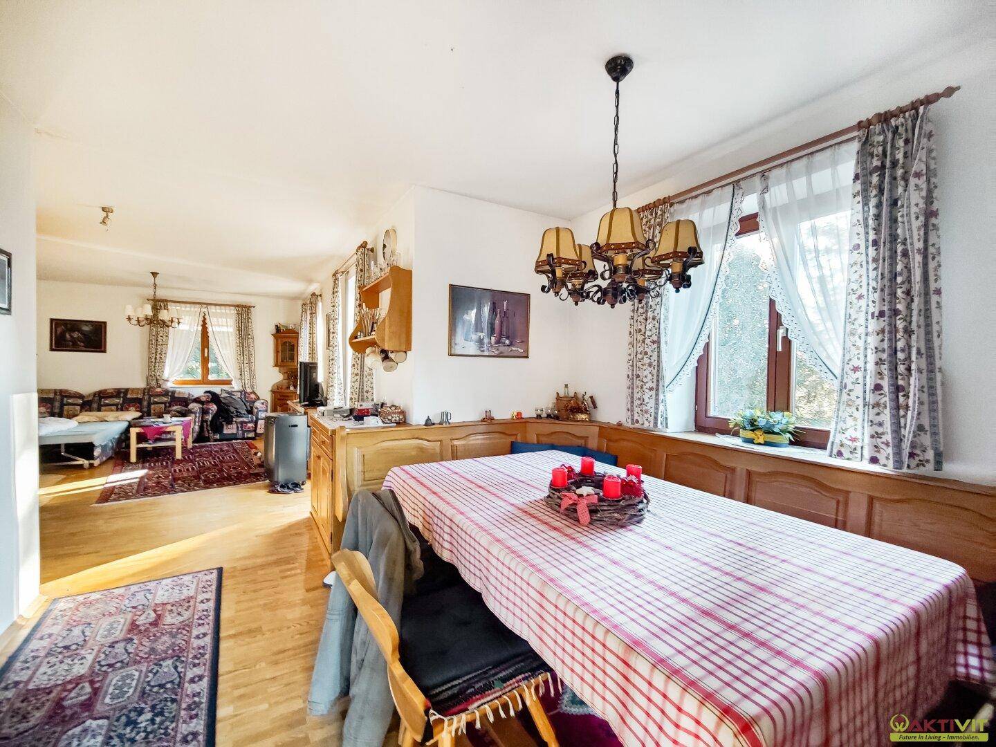 Essbereich mit Holzbänken und großem Tisch, offen zum Wohnzimmer mit Parkettboden.