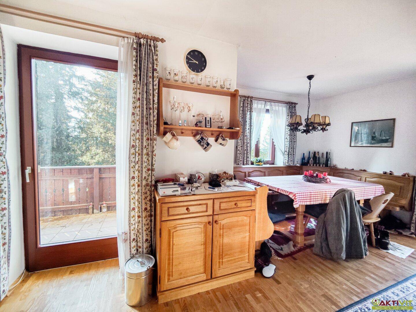 Heller Essbereich mit Zugang zum Balkon, Holzmöbeln und Blick ins Grüne.