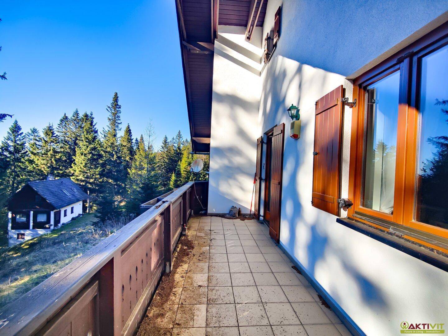 Geräumiger Balkon mit Fliesenboden und weitem Blick auf die bewaldete Landschaft.