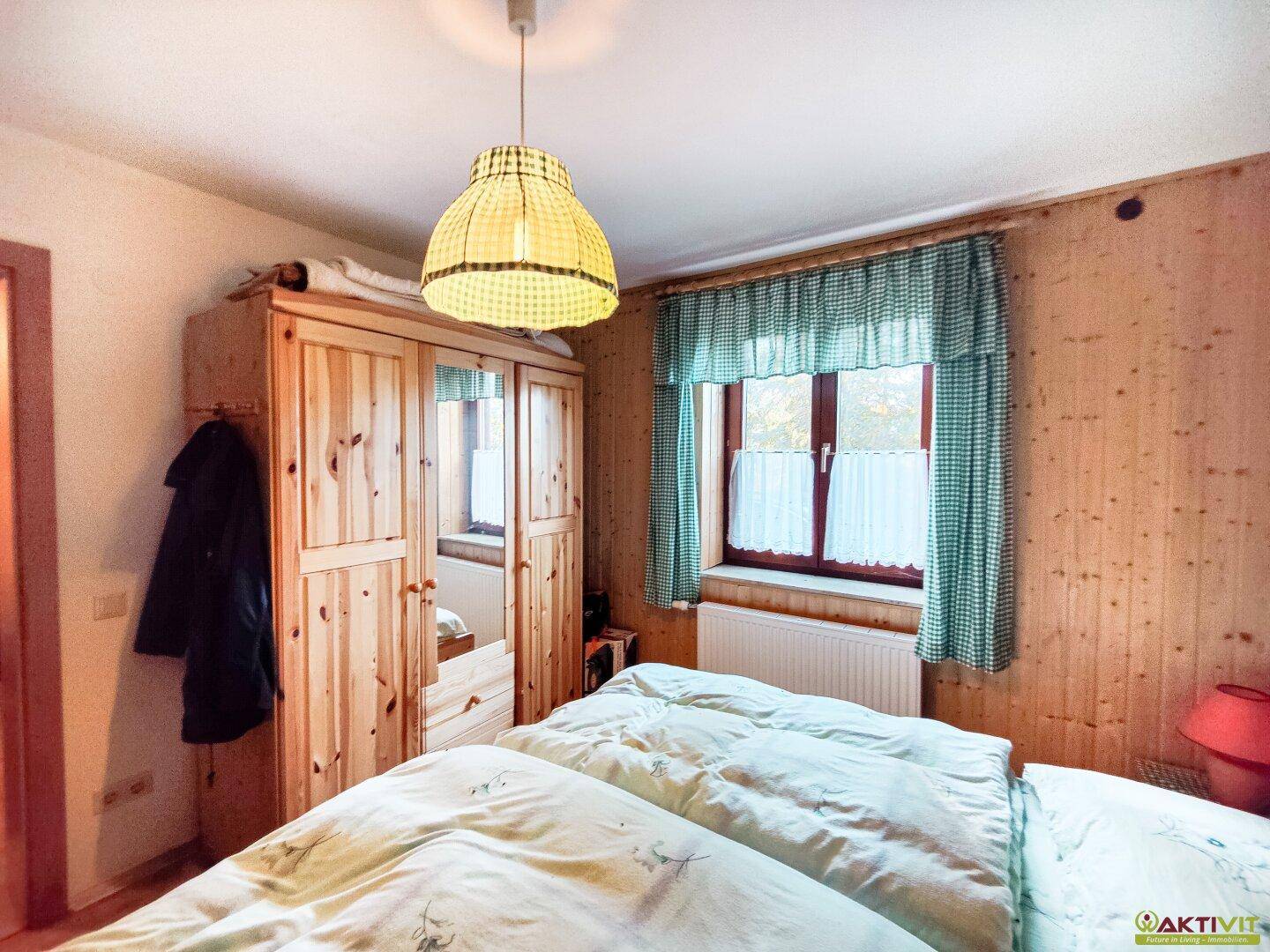 Helles Schlafzimmer mit Holzschrank, Doppelbett und karierten Vorhängen.