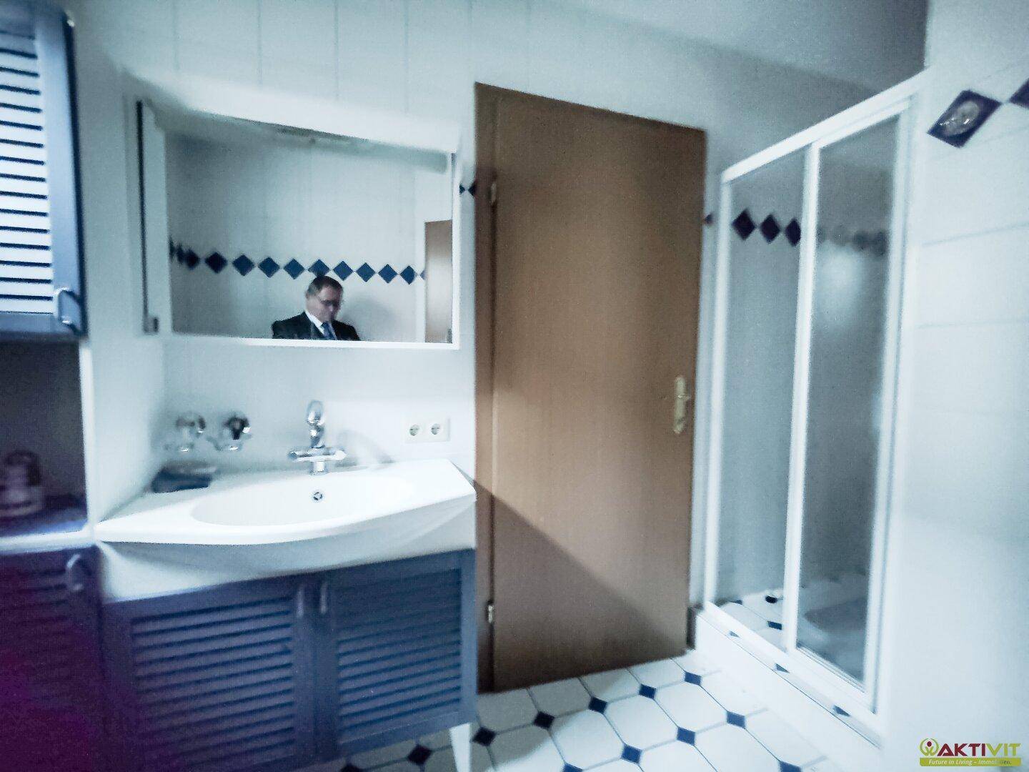 Badezimmer mit Waschbecken, Spiegelschrank und Duschkabine, gefliest in Weiß und Blau.